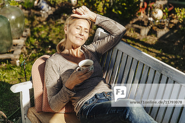Frau mit Tasse Kaffee entspannt auf der Gartenbank