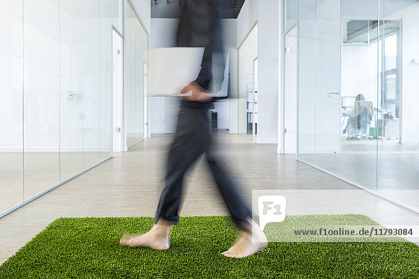 Ein reifer Geschäftsmann,  der barfuß auf einem Grasteppich im Büro läuft.