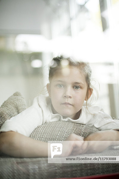 Porträt eines ernsthaften kleinen Mädchens  das aus dem Fenster schaut.
