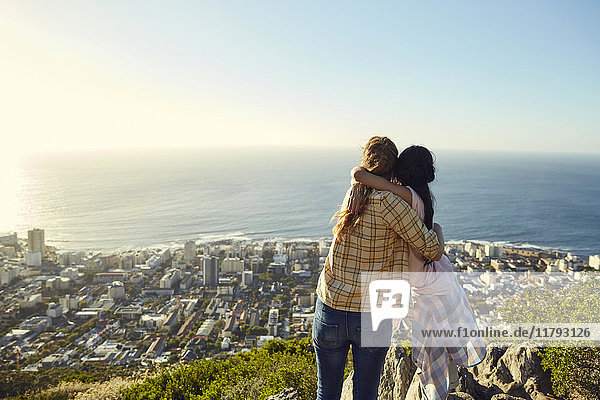 South Africa  Cape Town  Signal Hill  two young women hugging overlooking the city and the sea