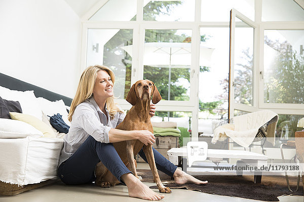 Relaxed woman sitting with her dog on floor of the living room