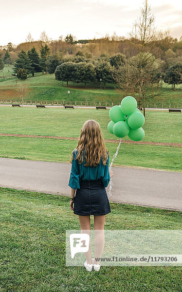 Back view of young woman with green balloons standing on a meadow