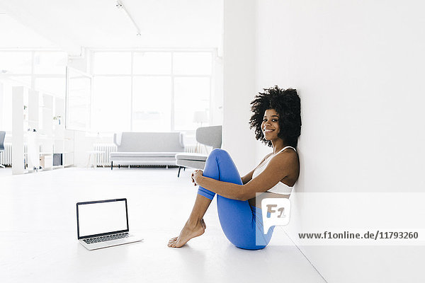 Fit young woman sitting on floor with laptop by her side