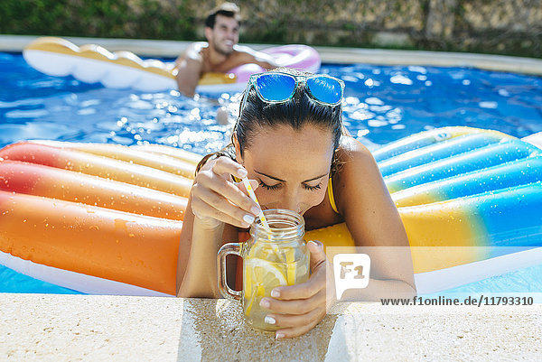 Young woman in swimming pool with drink at the poolside