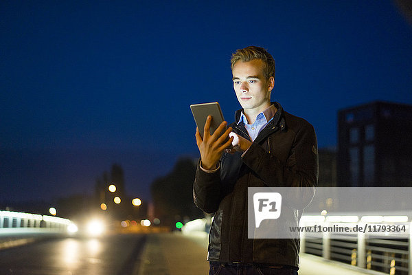 Junger Mann mit Tablette qutdoors in der Nacht
