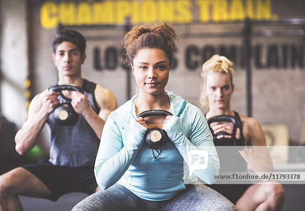 Selbstbewusste junge Frau mit Trainingspartnern beim Heben von Kettlebell im Fitnessstudio