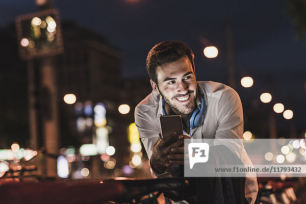 Smiling young man in the city with cell phone at night