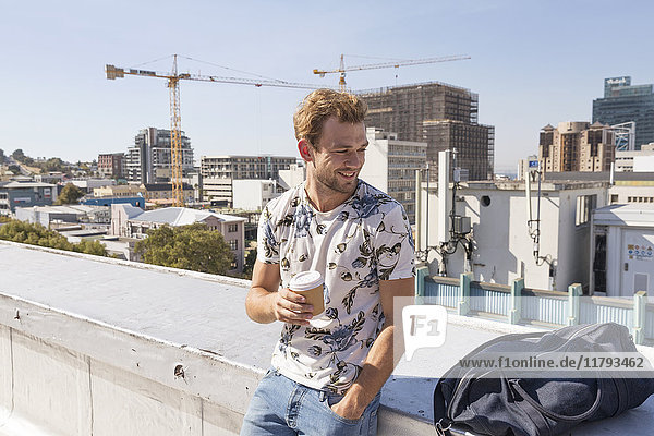 Young man standing on rooftop terrace drinking coffee