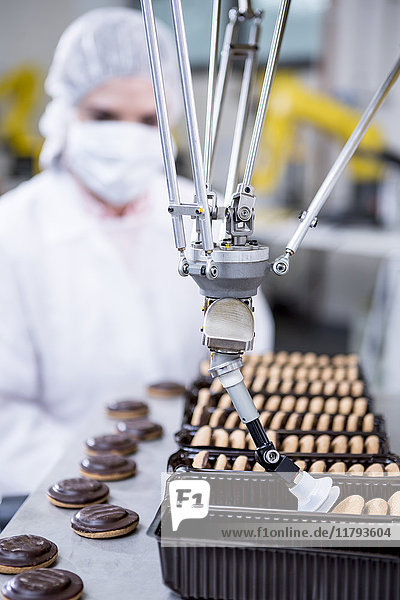 Frau in der Fabrik schaut sich den Roboter an  der Kekse handhabt