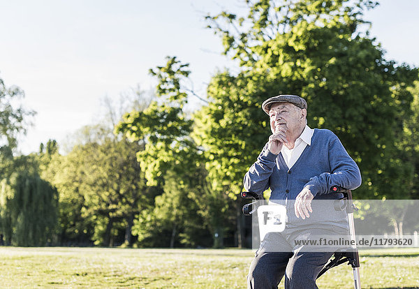 Nachdenklicher älterer Mann  der auf seinem Rollator in der Natur sitzt.
