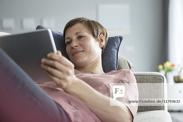 Porträt einer lächelnden Frau auf der Couch liegend mit Tablette