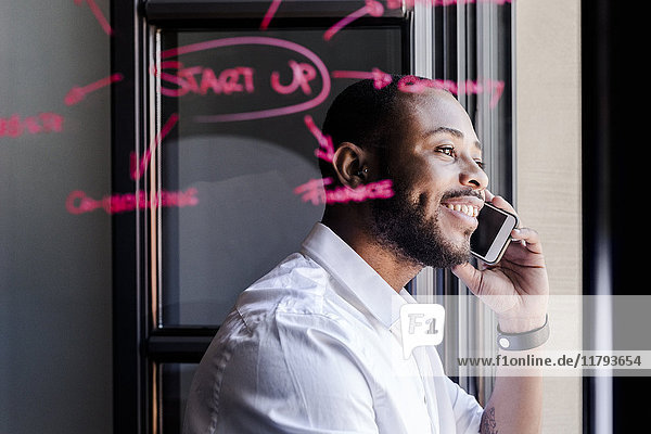 Lächelnder Geschäftsmann am Handy im Büro mit Schriftzug auf Fensterscheibe