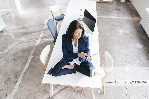 Geschäftsfrau sitzt auf dem Schreibtisch in einem Loft mit Tablette