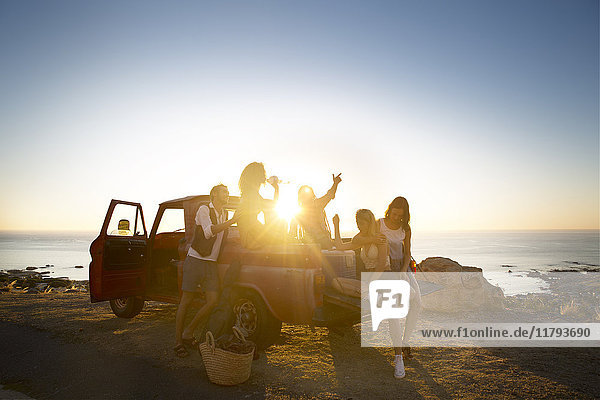 Fröhliche junge Leute draußen holen bei Sonnenuntergang den Lastwagen an der Küste ab.