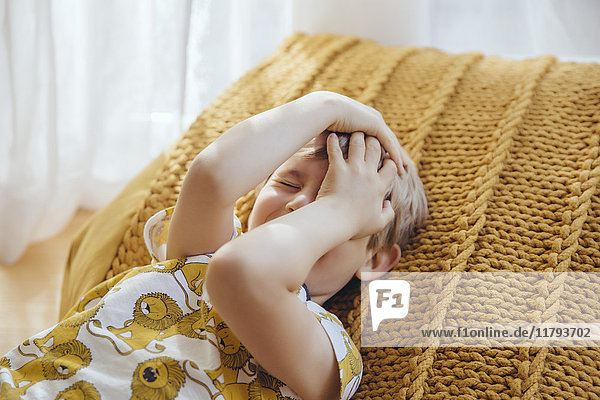 Little boy lying on cushion covering face with his hands