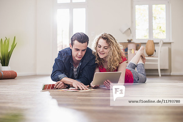 Young couple in new home lying on floor with tablet choosing from color sample