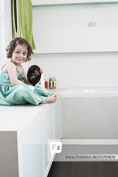Porträt des lächelnden Mädchens mit Handspiegel im Bad sitzend