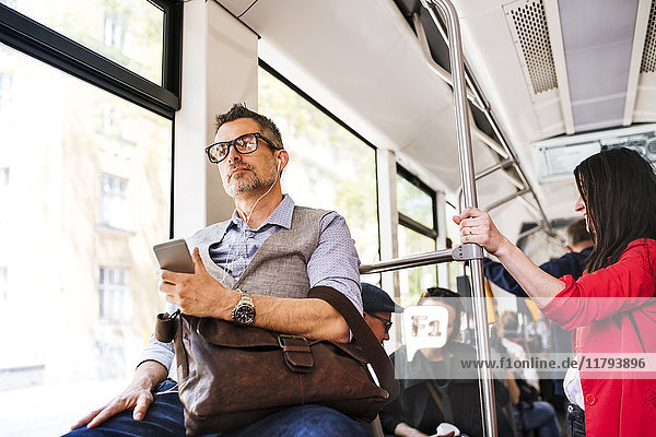 Geschäftsmann mit Smartphone und Kopfhörer  der in der Straßenbahn unterwegs ist.