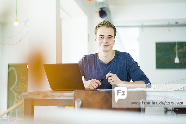 Porträt eines lächelnden Studenten bei der Arbeit mit dem Laptop