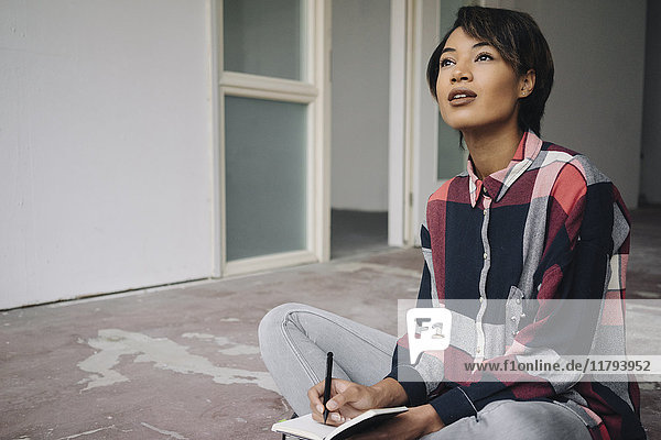 Frau sitzt auf gerissenem Boden mit Notizbuch