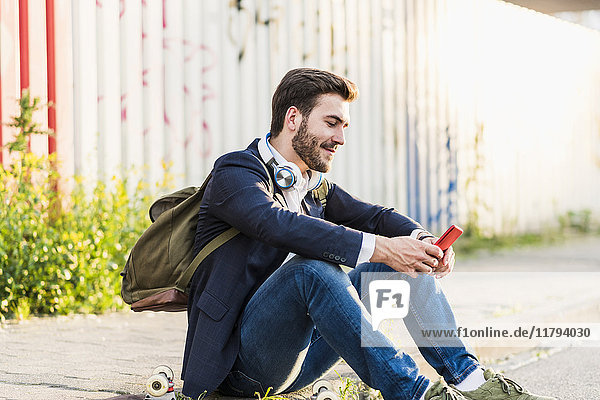 Smiling young man sitting on pavement checking cell phone