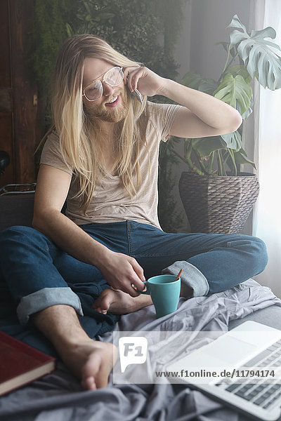 Man with long hair and beard using smartphone on sofa bed