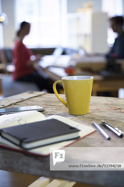 Notebook und Kaffeetasse im modernen informellen Büro mit Mann und Frau im Hintergrund