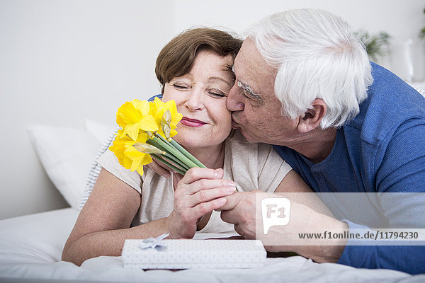 Seniorenpaar im Bett liegend  Mann schenkt Frau Blumenstrauß