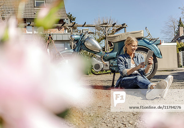 Smiling woman sitting at vintage motorcycle using tablet