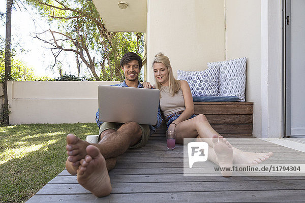 Lächelndes junges Paar auf der Terrasse sitzend mit Laptop