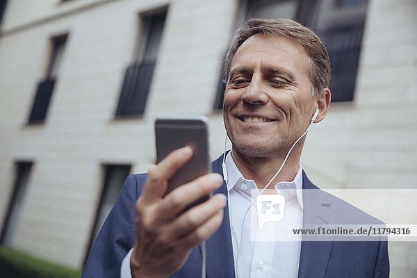Porträt eines lächelnden Geschäftsmannes im Freien mit Kopfhörer und Smartphone