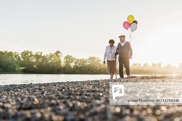 Seniorenpaar mit Ballons  die am Flussufer spazieren gehen