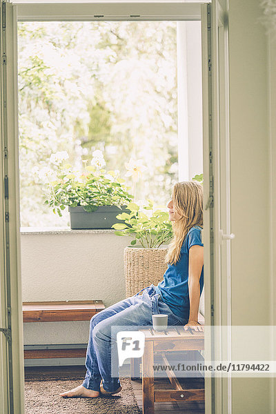 Entspannte junge Frau sitzend auf dem Balkon mit Tasse