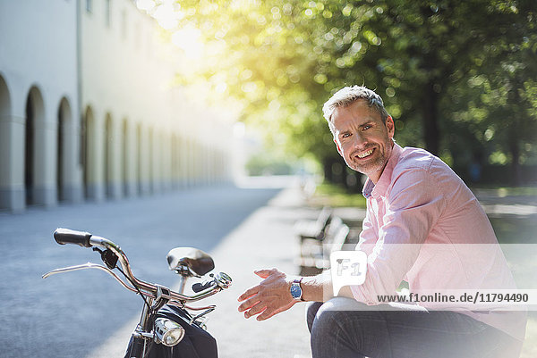 Porträt eines lächelnden Mannes mit Fahrrad auf der Parkbank