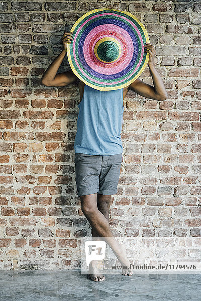 Man standing at brick wall covering his face with a sombrero