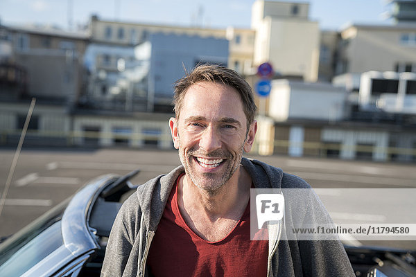 Porträt des lachenden reifen Mannes mit Stoppel vor seinem Sportwagen