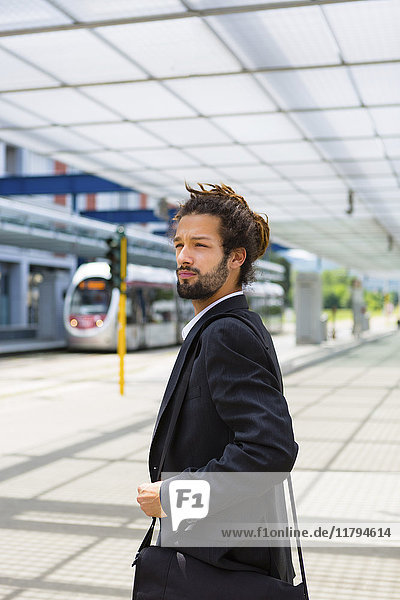Porträt eines jungen Geschäftsmannes mit Rastalocken am Bahnhof