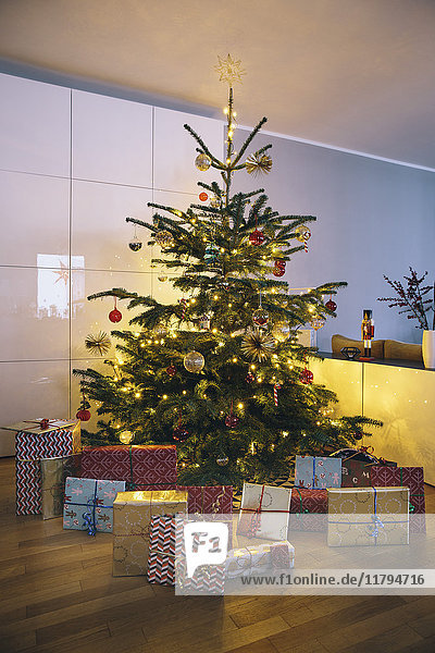 Dekorierter Weihnachtsbaum im Wohnzimmer mit Weihnachtsgeschenken im Vordergrund