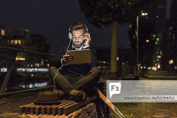 Young man with tablet and headphones in the city at night