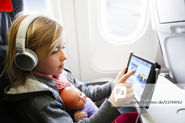 Little girl sitting on an airplane watching something on digital tablet