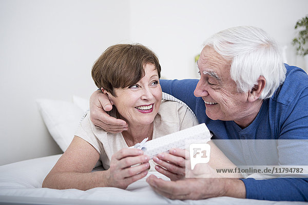 Seniorenpaar im Bett liegend  Mann verschenkt Frau