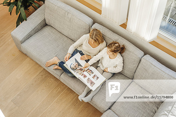 Mature woman and girl at home looking at photo album on couch