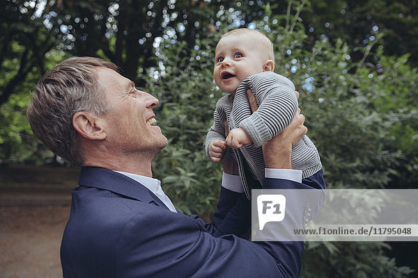 Happy mature businessman holding up baby boy outdoors