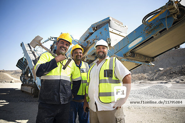 Colleague workers at quarry standing in front of digger