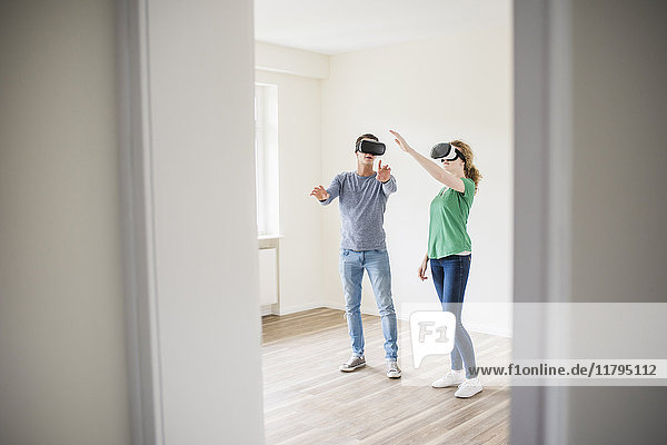 Young couple discussing in empty apartment wearing VR glasses