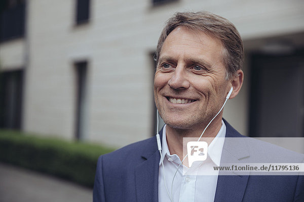 Porträt eines lächelnden Geschäftsmannes im Freien mit Kopfhörern