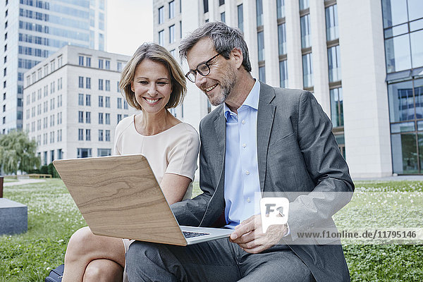 Smiling businesswoman and businessman sharing laptop outdoors