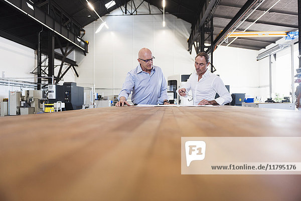 Zwei Geschäftsleute betrachten den Plan auf dem Tisch in der Fabrik