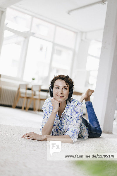 Woman lying on floor in her apartment  wearing headphones