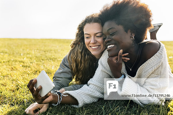 Two best friends lying in grass with cell phone
